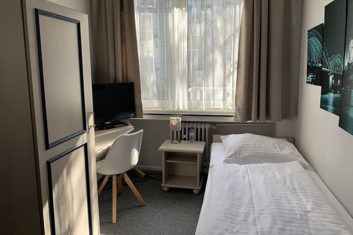 Habitación de hotel con cama, escritorio, computadora, silla y ventana con cortinas.