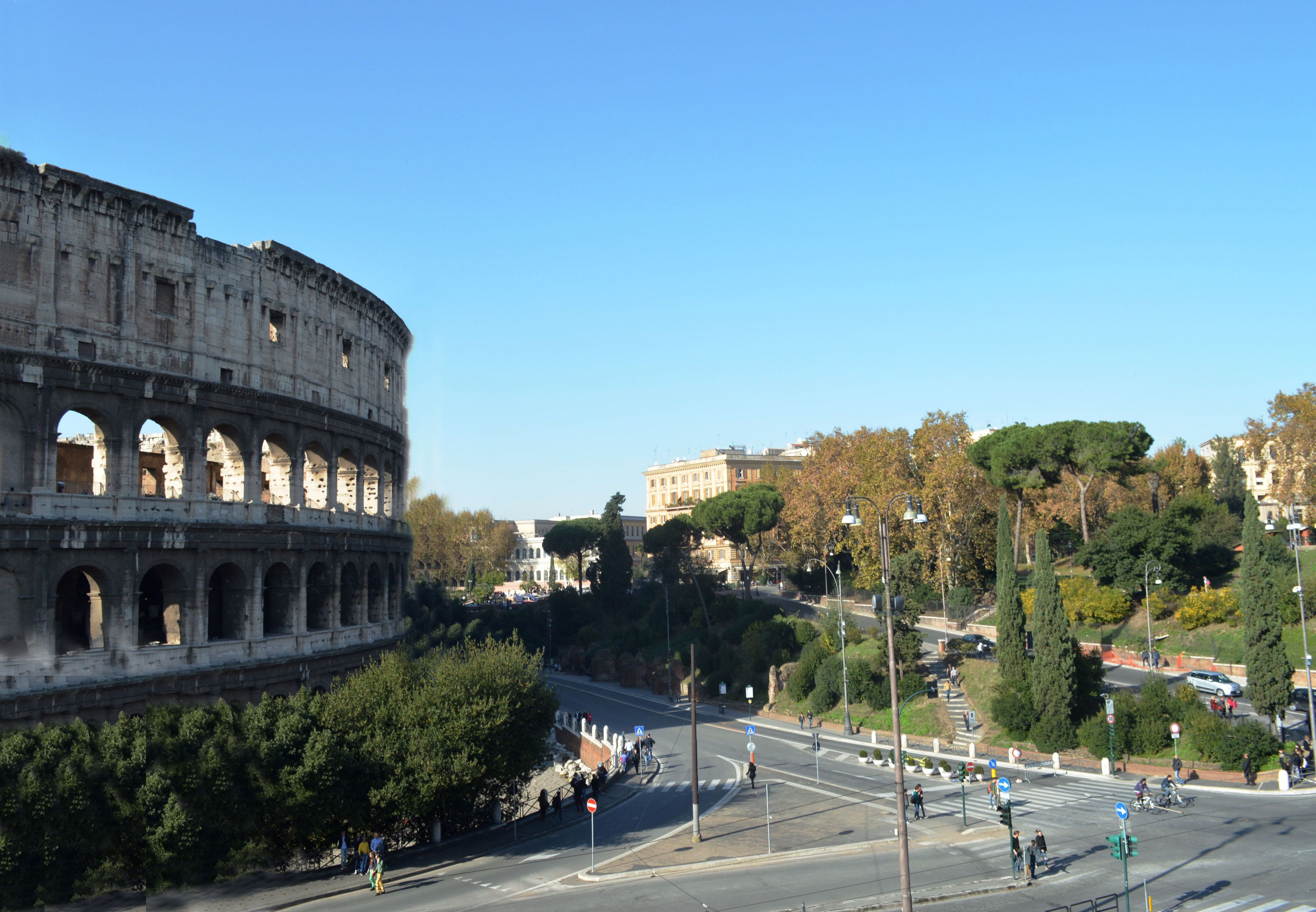 A view of the Colosseum with a road in the foreground and buildings in the background.