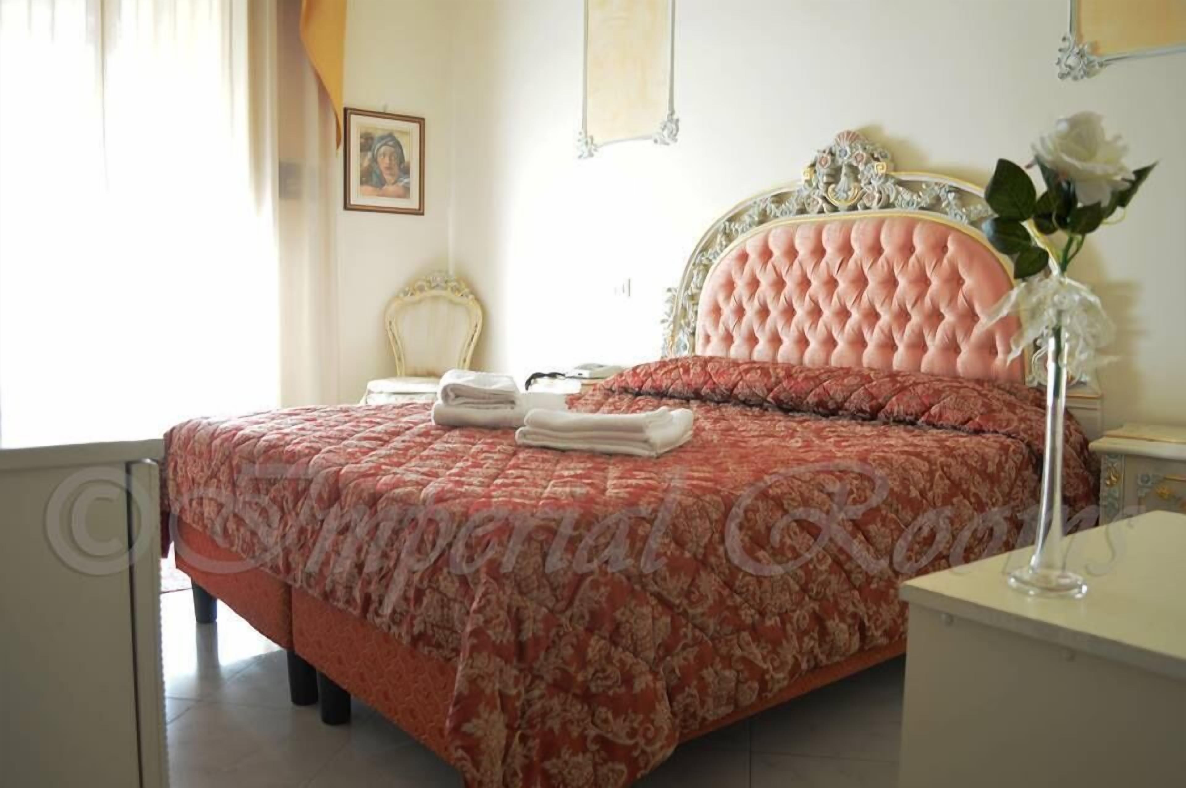 Un dormitorio con una cama grande, una mesita de noche, una silla y un jarrón con flores.