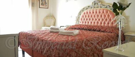 Un dormitorio con una cama grande, una mesita de noche, una silla y un jarrón con flores.