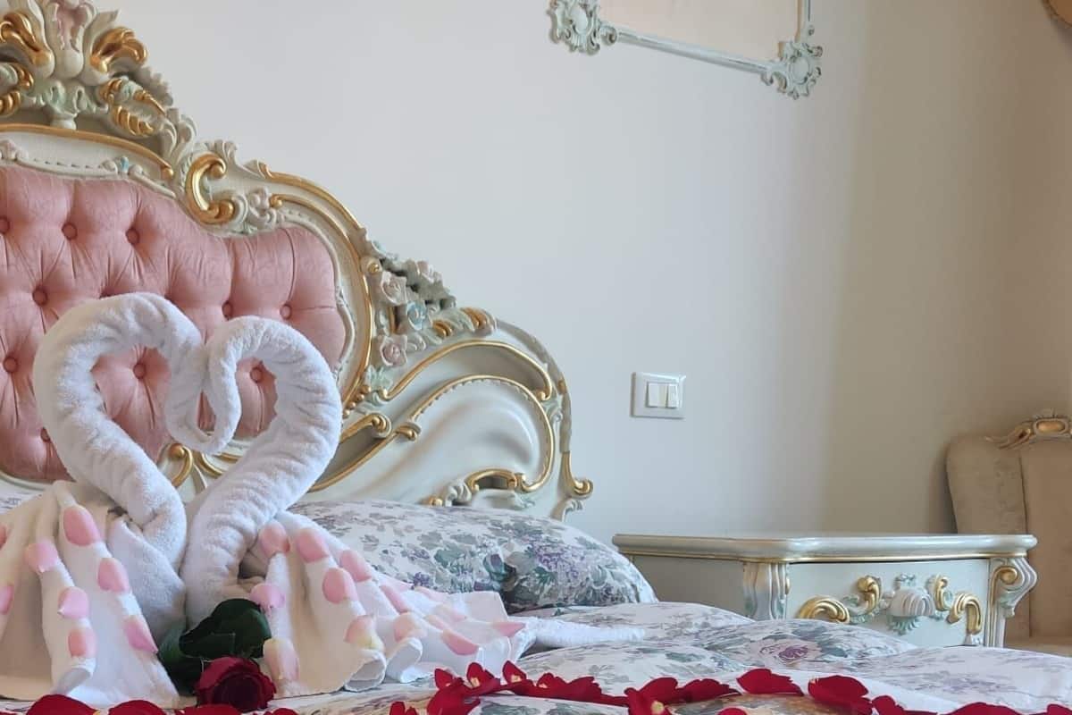 A bed with a heart-shaped tufted headboard, a floral bedspread, and a decorative wall-mounted light fixture.