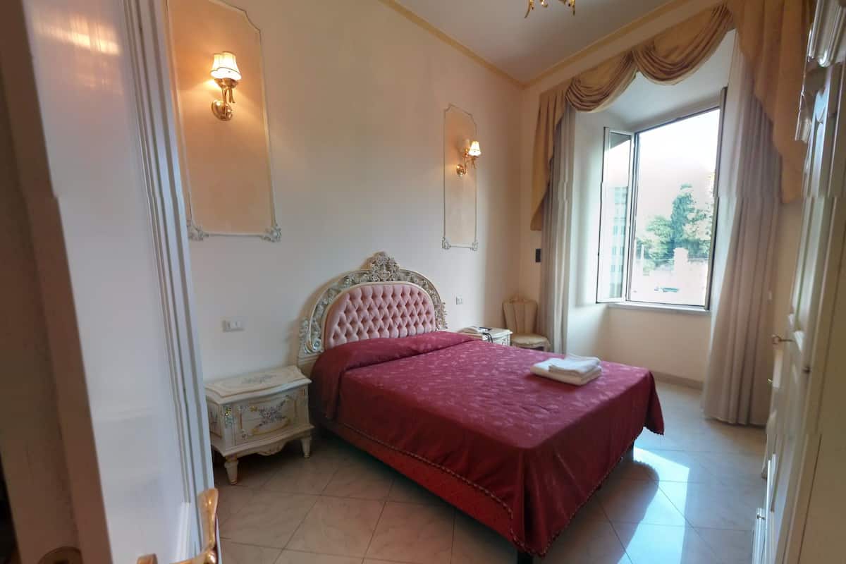 A bedroom with a large bed, two bedside tables, a nightstand, a window with curtains, and wall-mounted lamps.