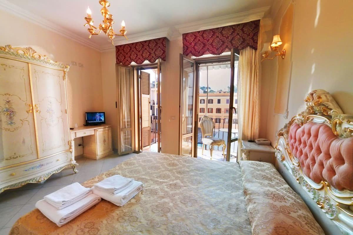 A bedroom with a large bed, a TV, a wardrobe, and a balcony with a chair.