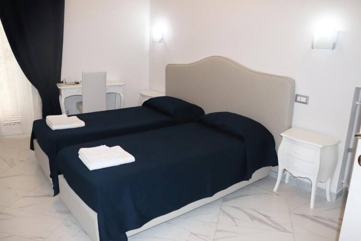 A hotel room with two beds, a desk, a chair, a nightstand, and a bathroom door.