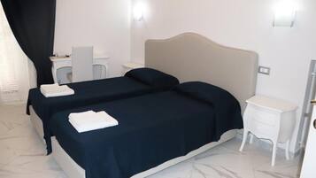 Habitación de hotel con dos camas, un escritorio, una silla, una mesita de noche y la puerta del baño.