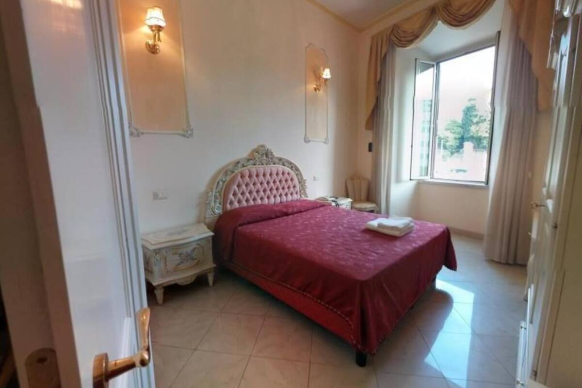 A bedroom with a bed, nightstand, wall sconces, and a window with curtains.