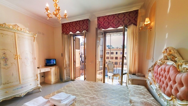 A spacious bedroom with a large bed, a television, and a balcony with a chair. - Imperial Rooms (Rome)