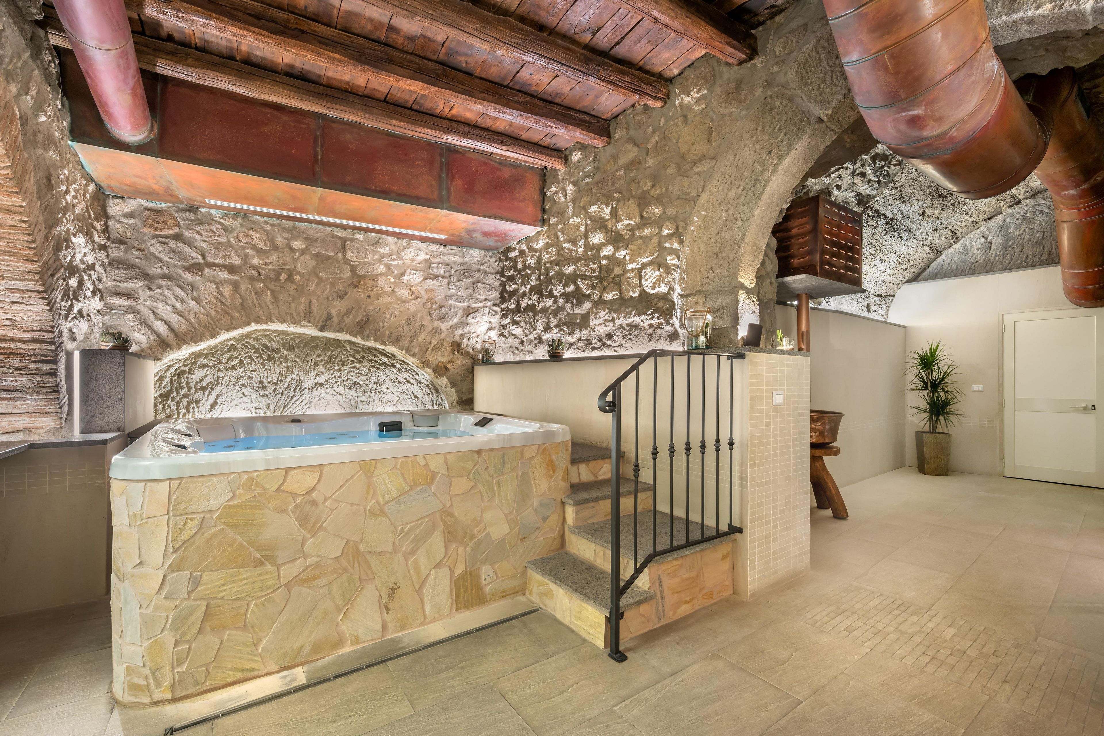 Une salle de bain aux murs en pierre, dotée d’une baignoire, d’une douche et d’un escalier en bois.