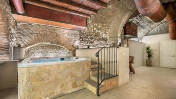 Une salle de bain aux murs en pierre, dotée d’une baignoire, d’une douche et d’un escalier en bois.