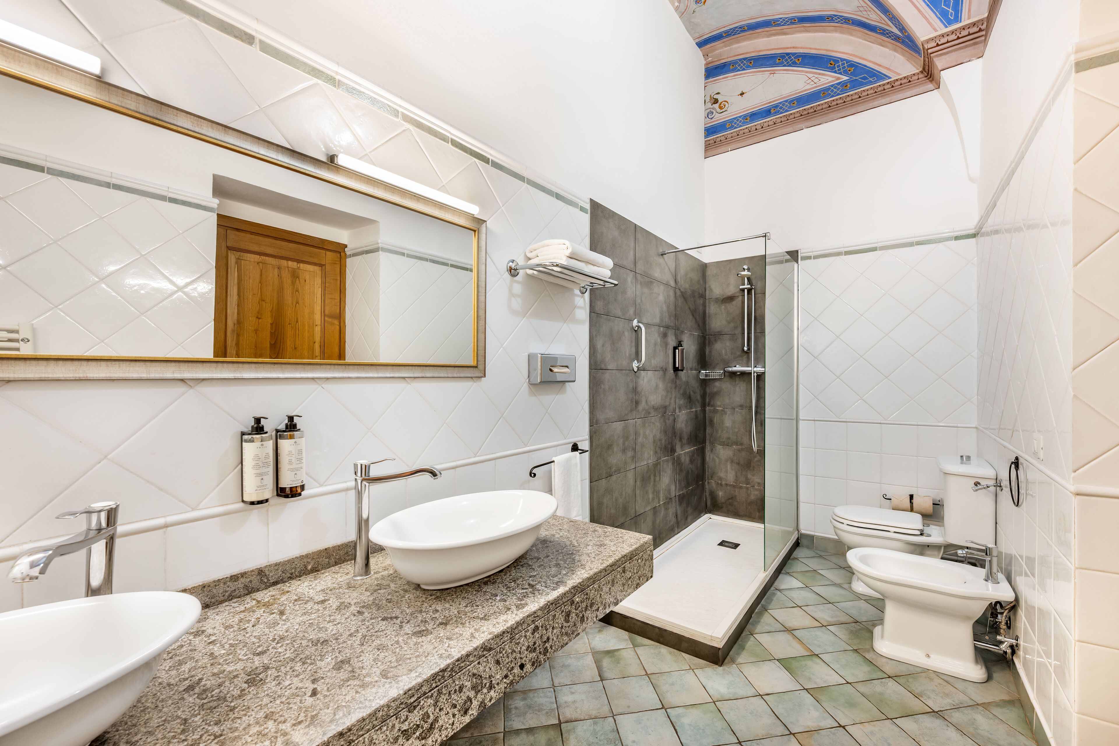 Un baño con un espejo grande, dos lavamanos, ducha y retrete.