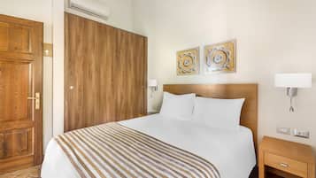 A hotel room with a large bed, wooden wardrobe, two wall-mounted lamps, and two decorative wall pieces.