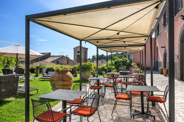 Un patio al aire libre con mesas y sillas, una zona cubierta y un edificio de piedra al fondo.