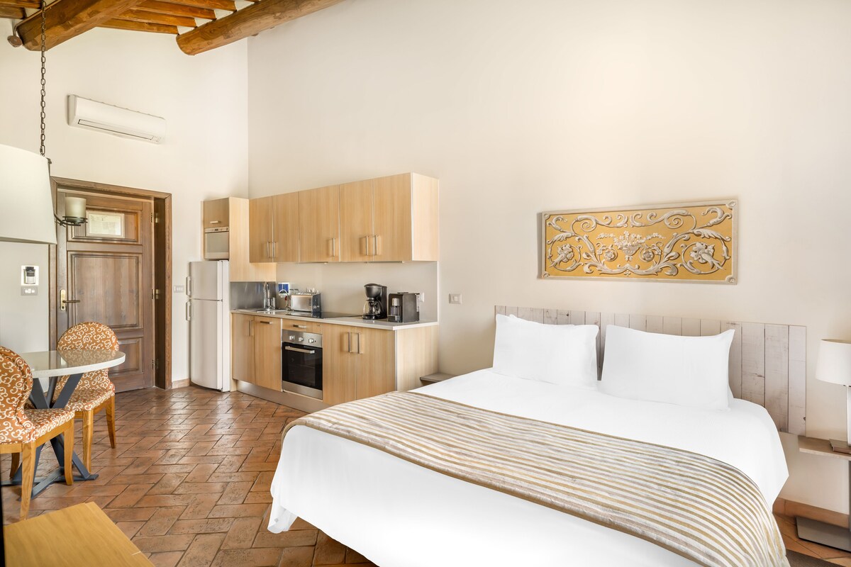 Habitación de hotel con cama, zona de comedor con sillas, kitchenette y un adorno decorativo en la pared.