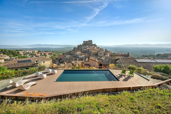 Una piscina en la azotea con sillas de descanso, vista a un pueblo histórico con un castillo y follaje circundante.