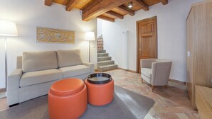 A living room with a sofa, ottoman, and a chair, wooden beams on the ceiling, a staircase, and a door. - Hilton Vacation Club Palazzo Catalani & Soriano (Soriano nel Cimino)