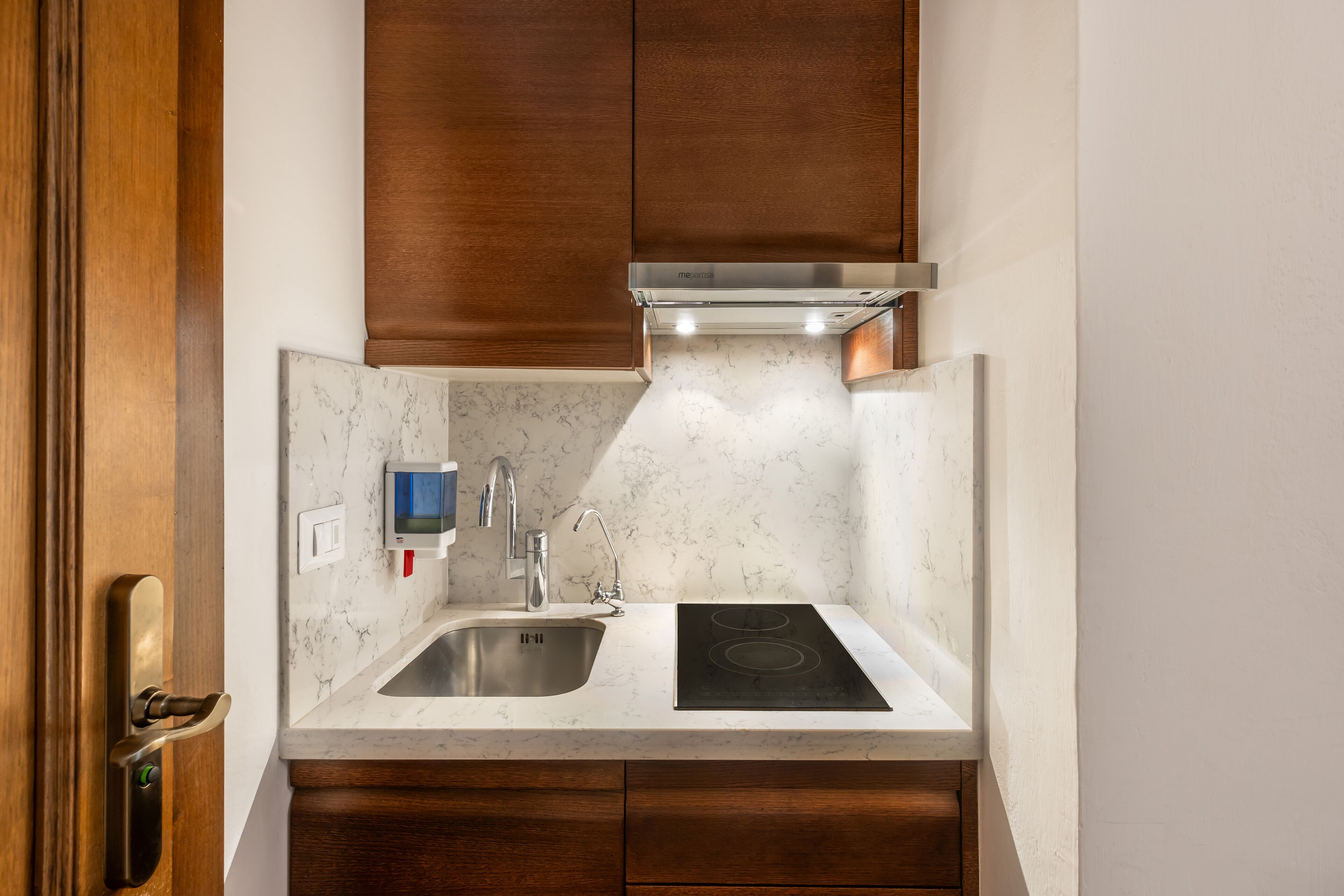 Una cocina compacta con pileta integrada, estufa y grifo de pared.