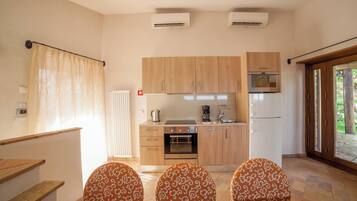 A compact kitchen with wooden cabinets, a built-in oven, and a refrigerator. There are two patterned chairs and a window with curtains.