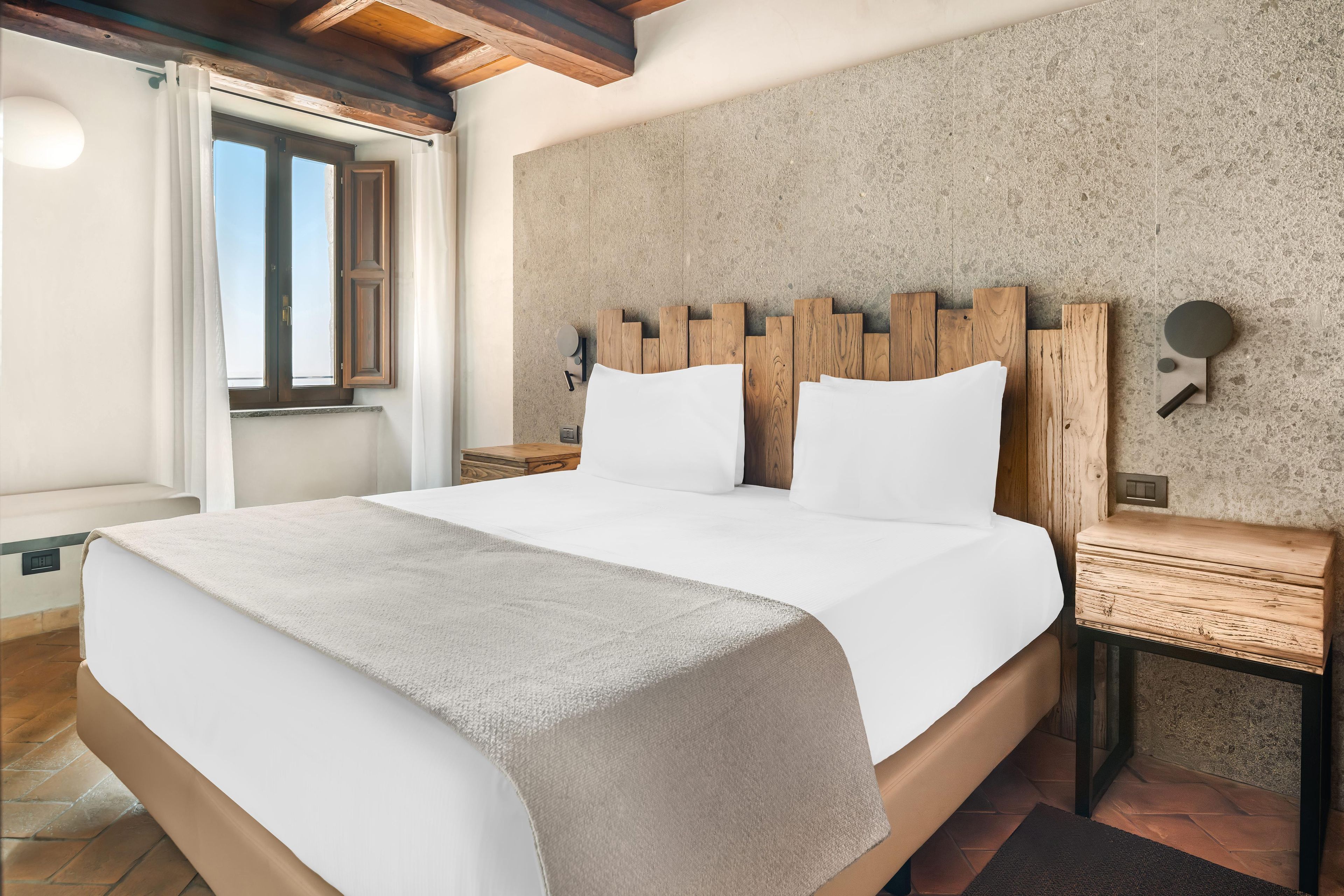 Una habitación de hotel con una cama grande, cabecera de madera, una mesita de noche y una lámpara de pared.