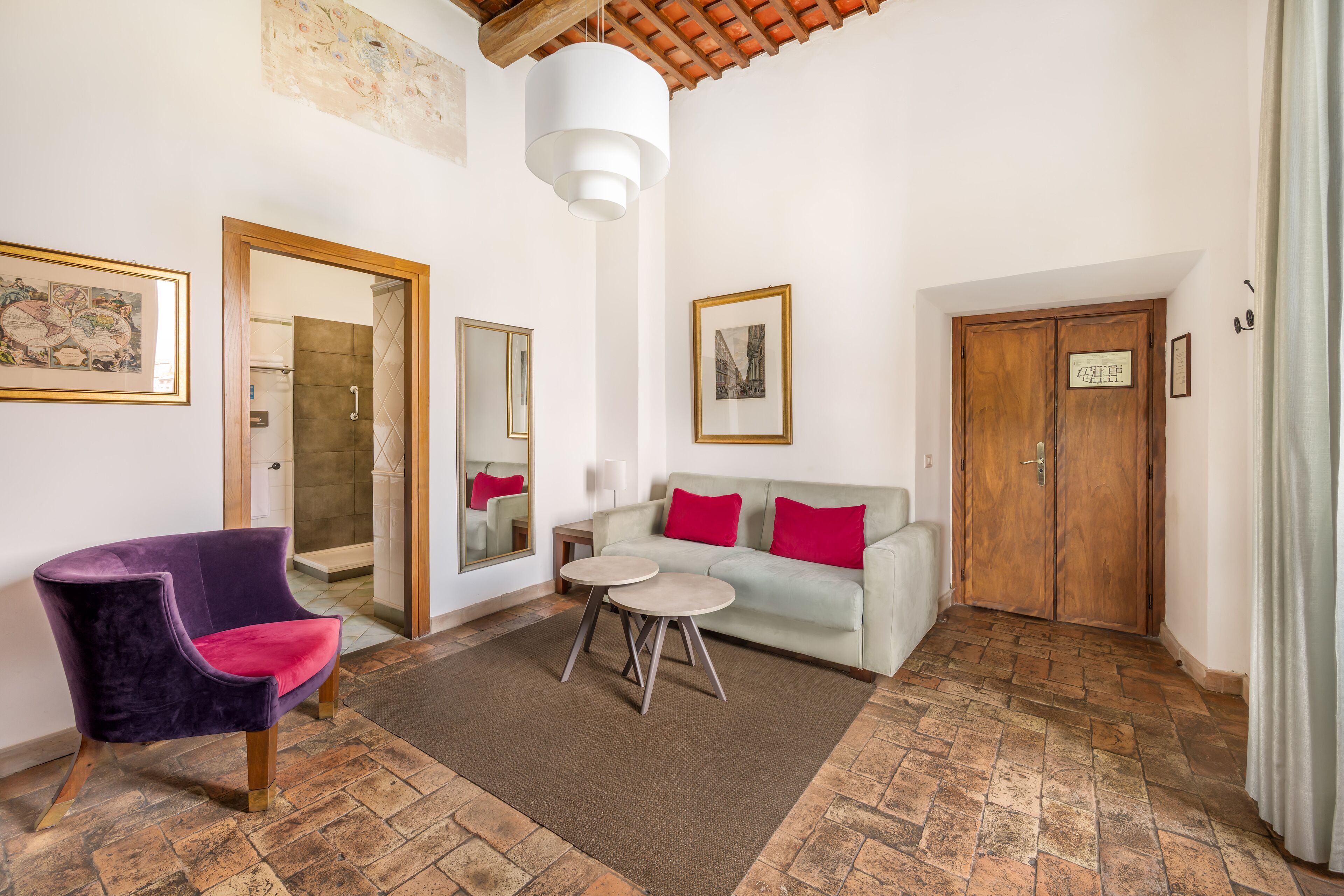A room with a purple chair, a white sofa with red cushions, a small round table, and a wooden door.