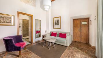 A room with a purple chair, a white sofa with red cushions, a small round table, and a wooden door.