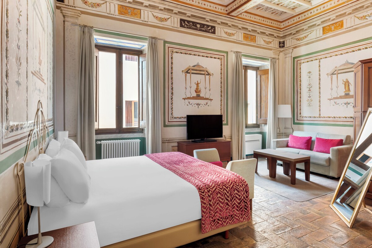 Una habitación de hotel con cama, televisor, sofá y mesa de comedor.