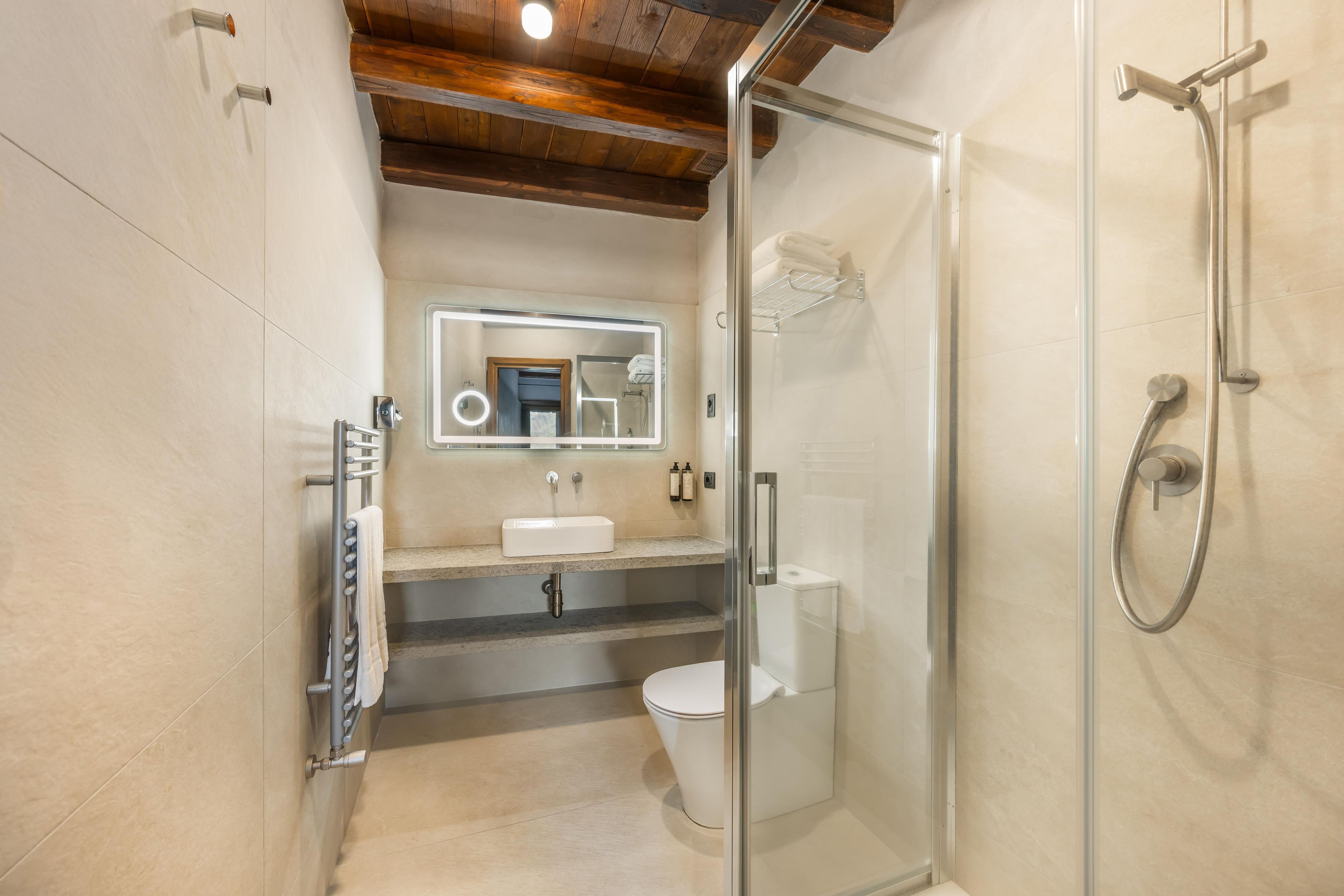 A modern bathroom with a glass-enclosed shower, a white sink, and a mirror with a light above it.