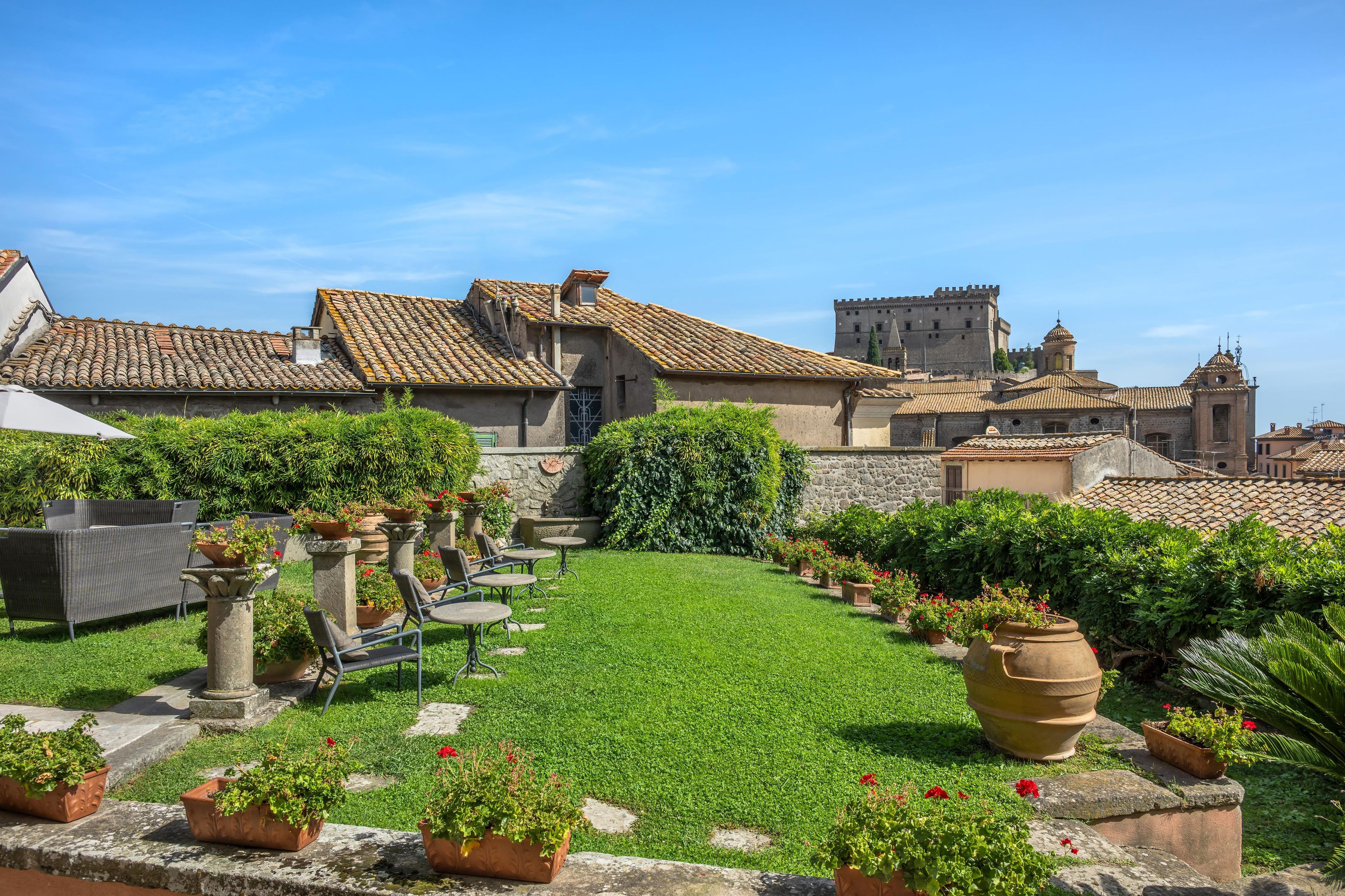 A courtyard with a grassy area, potted plants, outdoor furniture, and historic buildings with tiled roofs.