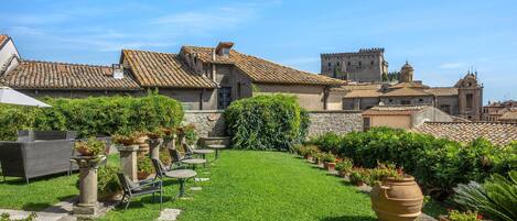 A courtyard with a grassy area, potted plants, outdoor furniture, and historic buildings with tiled roofs.