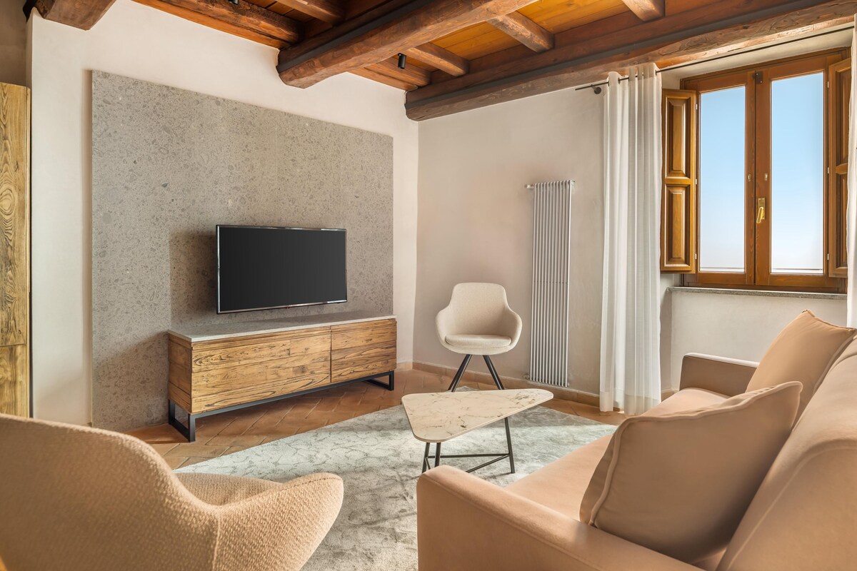 Una sala de estar con televisor sobre un mueble de madera, una silla blanca y un sofá.