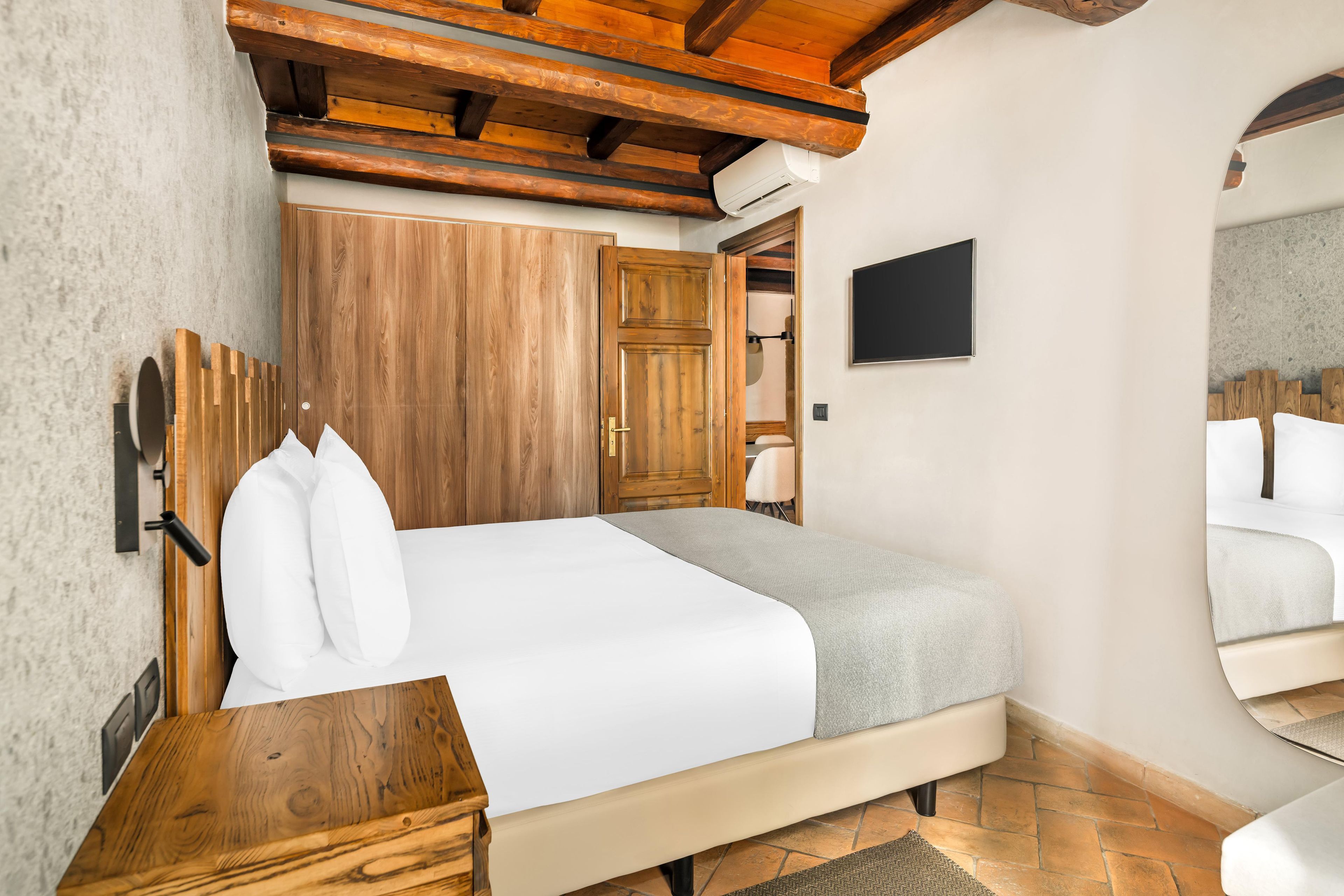 Ein Schlafzimmer mit einem Holzschrank, einem Bett mit weißer Bettwäsche, einem kleinen Tisch und einem an der Wand befestigten Fernseher.