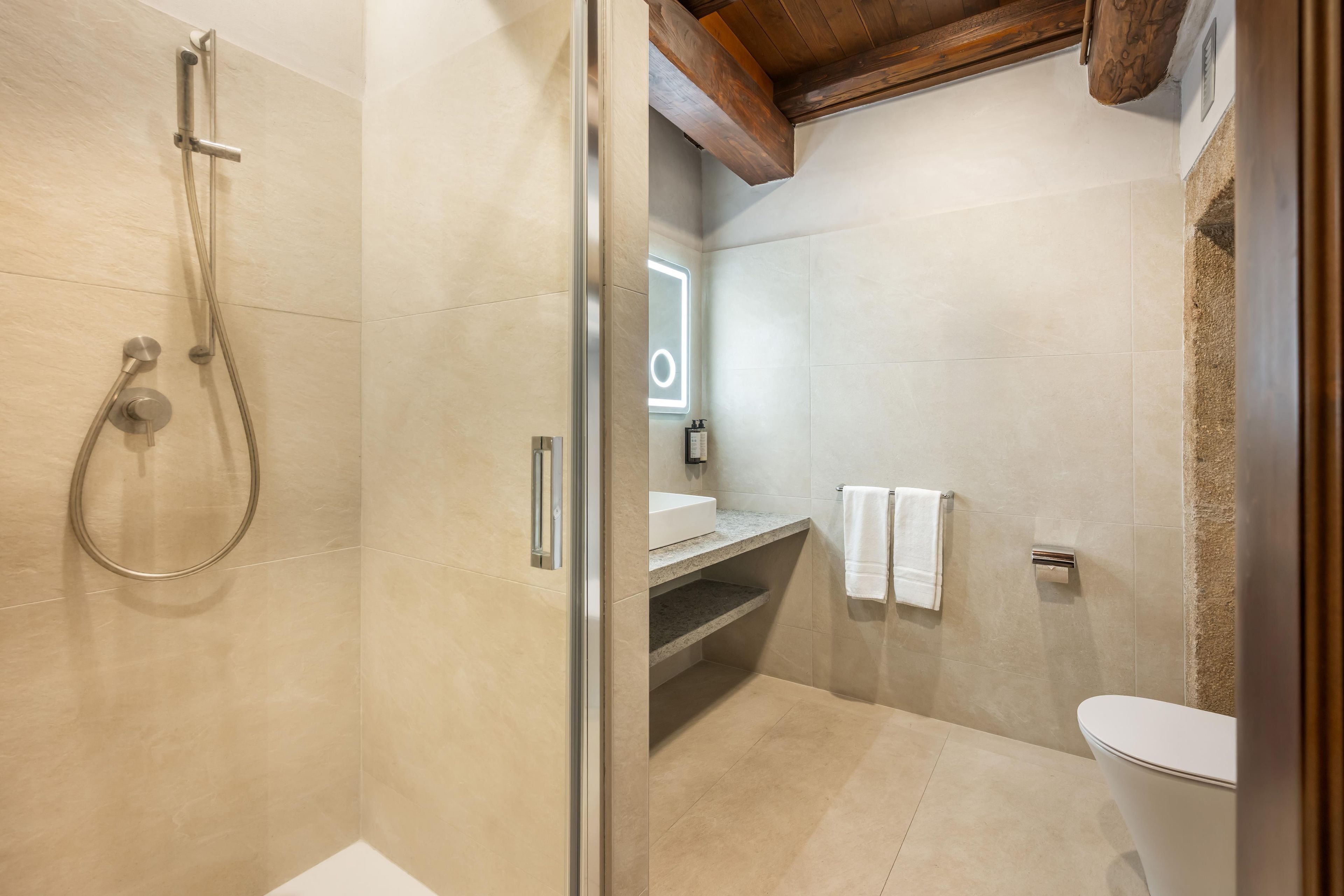 A modern bathroom with a glass-enclosed shower, a toilet, and a sink with a towel rack.
