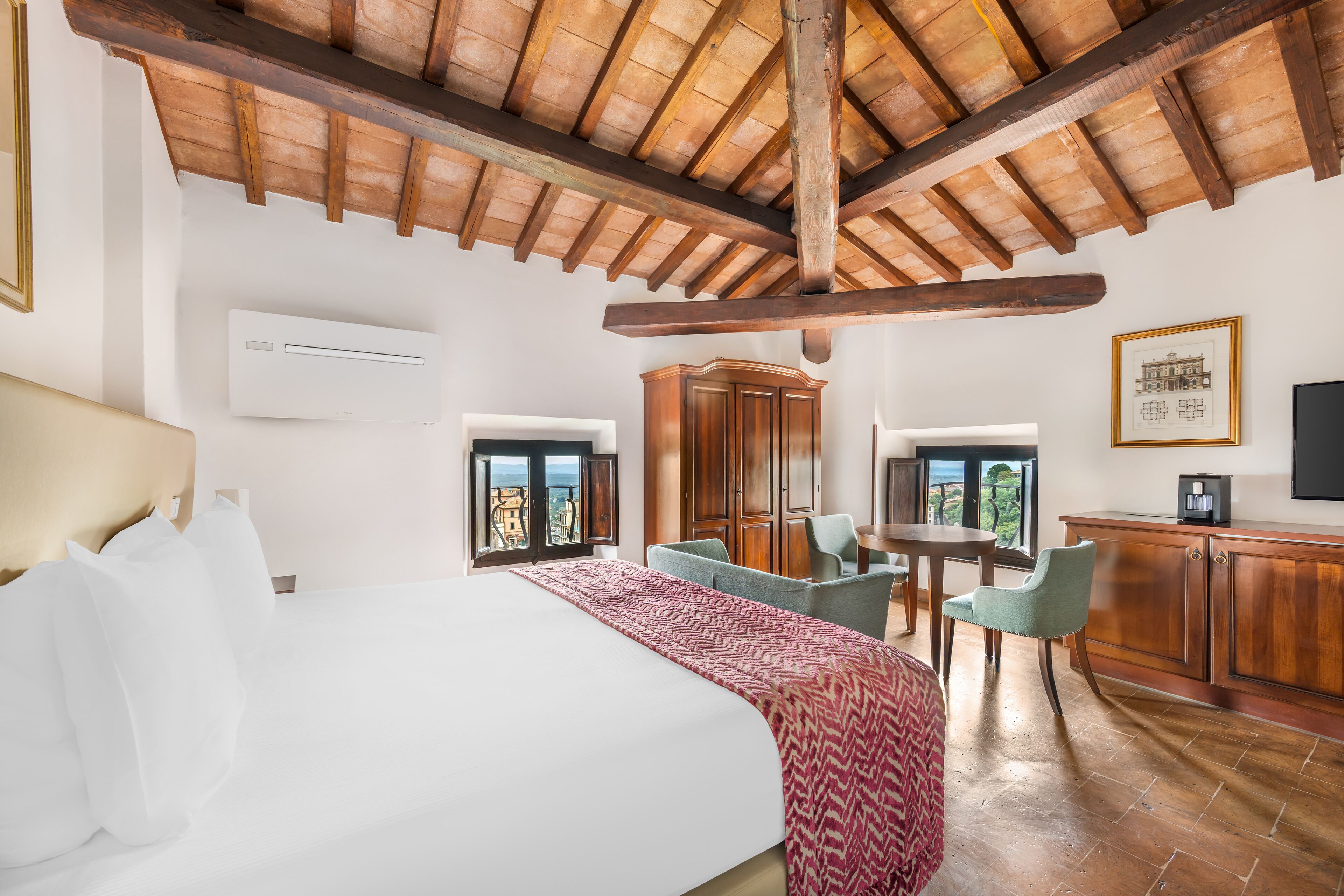 Habitación de hotel con una cama grande, vigas de madera en el techo, un comedor con sillas y vistas a través de las ventanas.