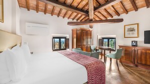 A hotel room with a large bed, wooden ceiling beams, a dining area with chairs, and a view through the windows. - Hilton Vacation Club Palazzo Catalani & Soriano (Soriano nel Cimino)