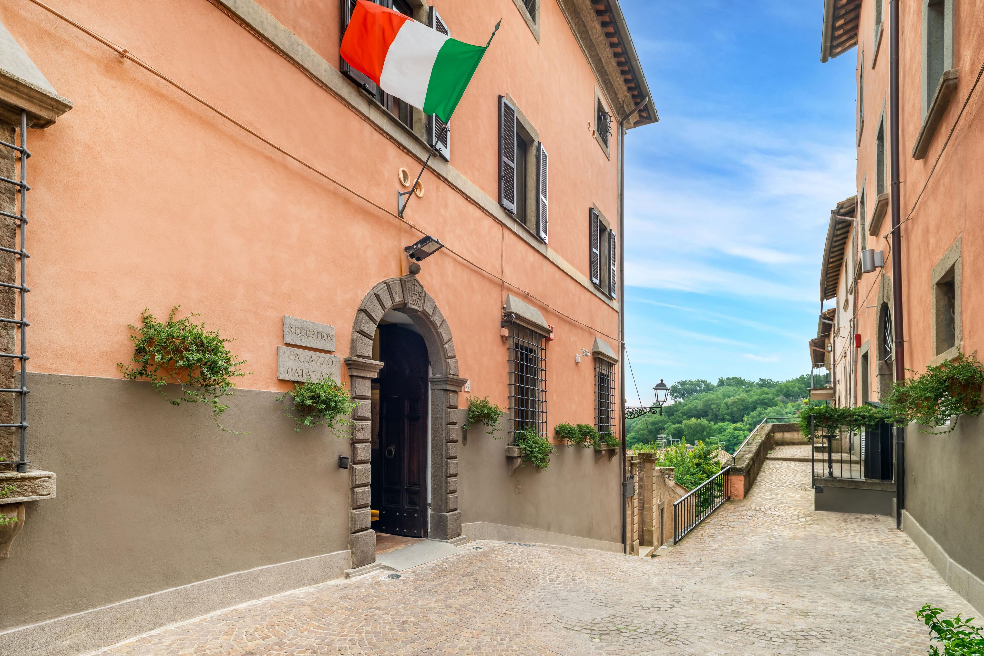 A cobblestone street leading to a building with a sign reading 'RECEPTION' and 'PALAZZO CATALAN'.