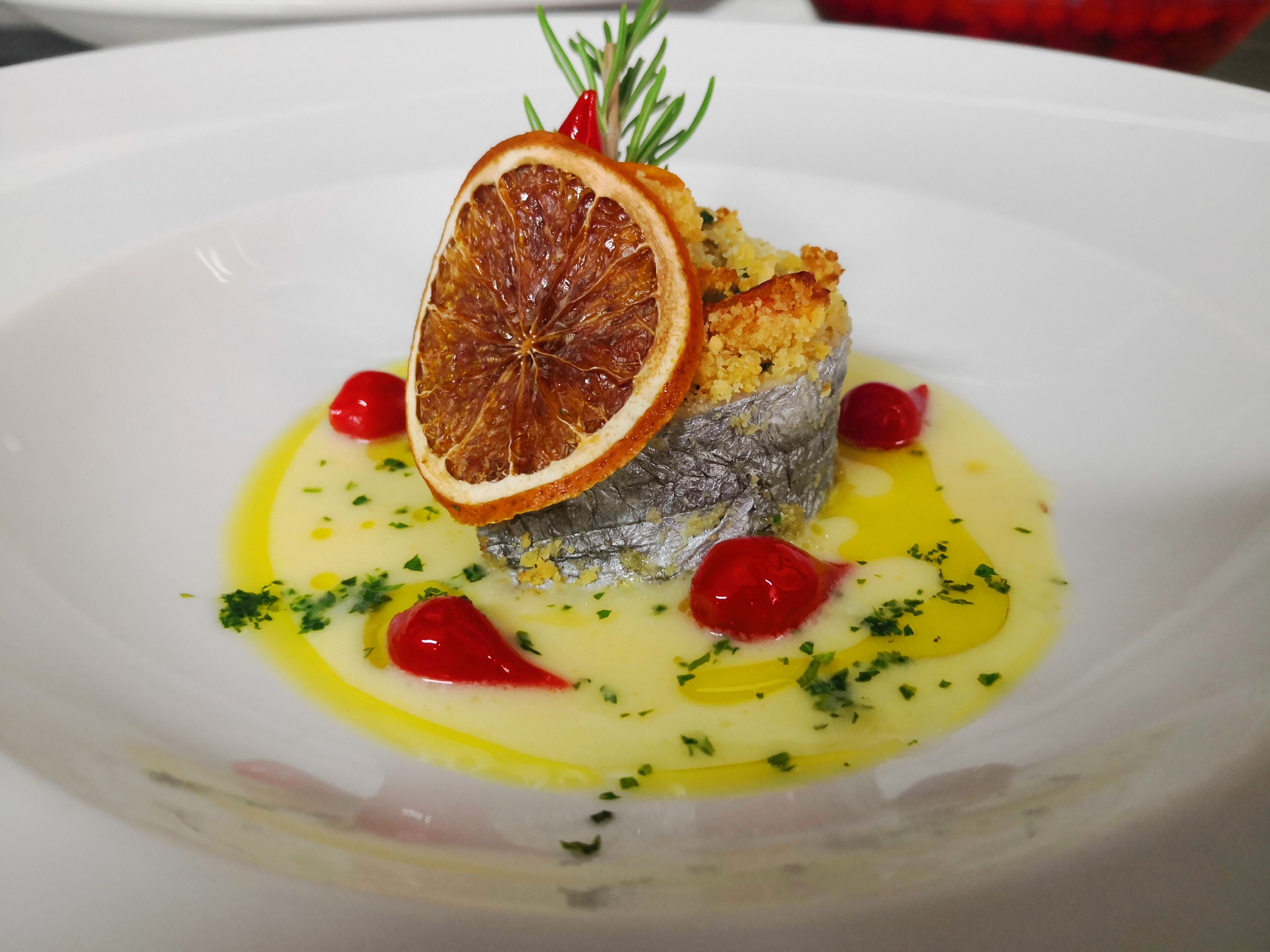 Un plato con un pescado, una rodaja de naranja deshidratada y bayas rojas.