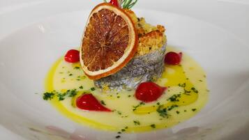 Un plato con un pescado, una rodaja de naranja deshidratada y bayas rojas.