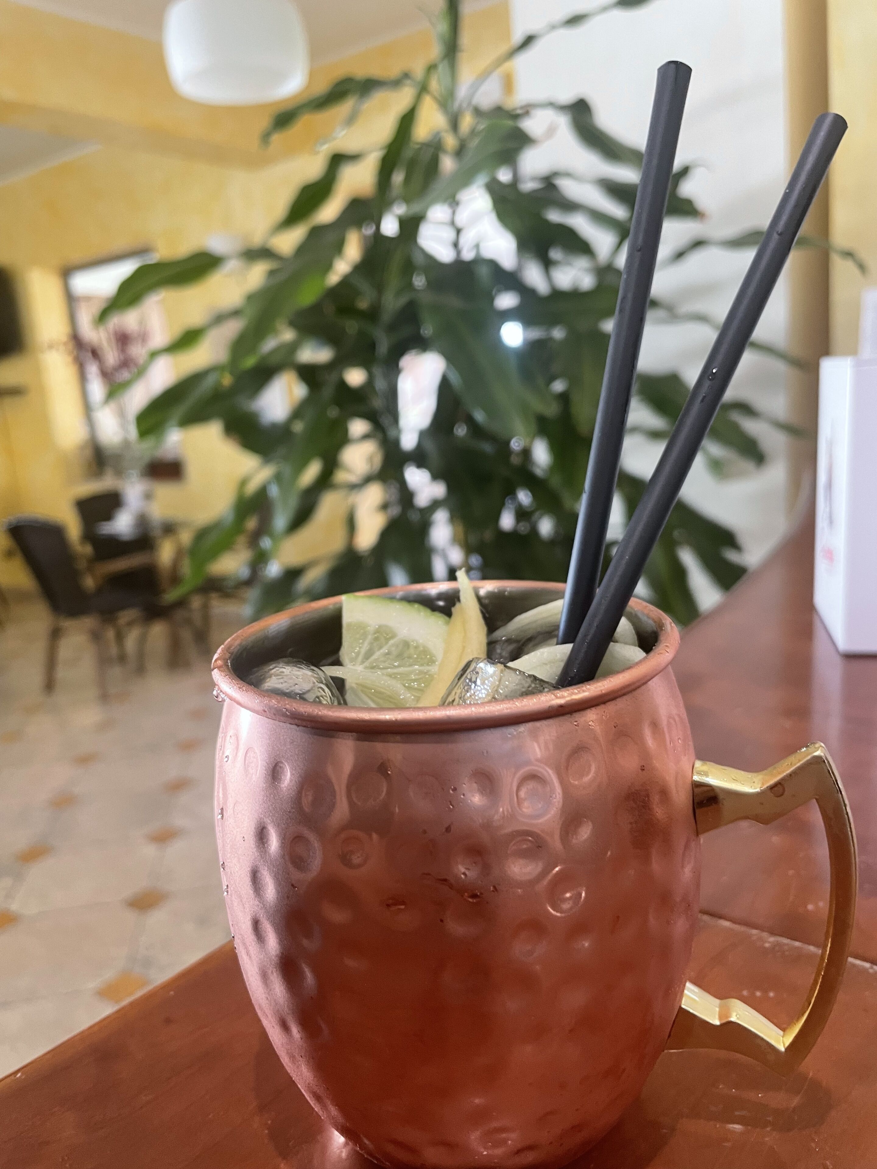 Eine kupferne Tasse mit Henkel, gefüllt mit Eiswürfeln und Limettenscheiben, steht auf einem Tisch.