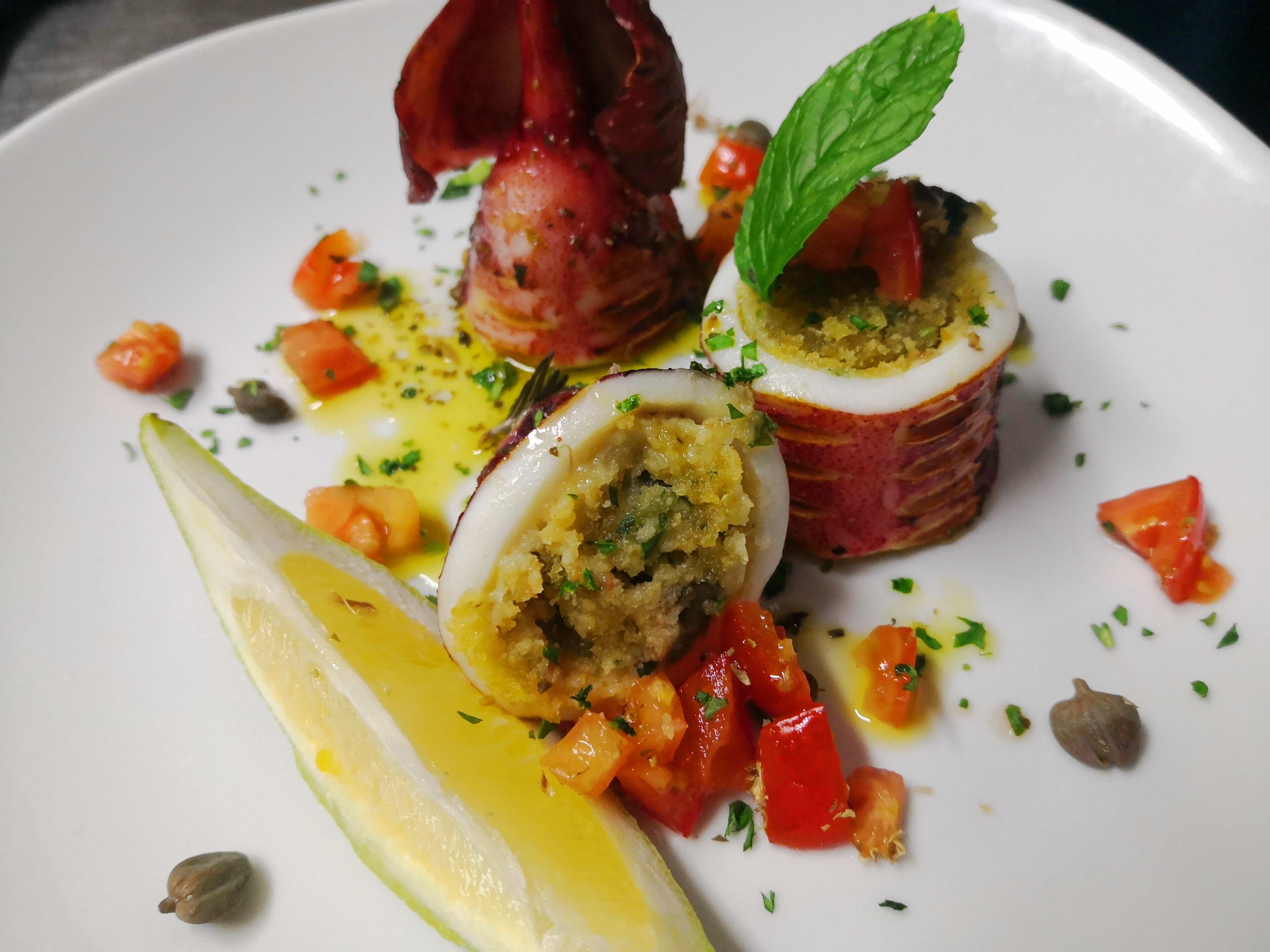 Un plato de comida con una cuña de limón, un champiñón relleno y una guarnición de hierbas.