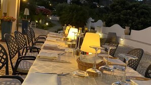 Un área de comedor al aire libre con mesas dispuestas para una comida, sillas y vistas a una colina.