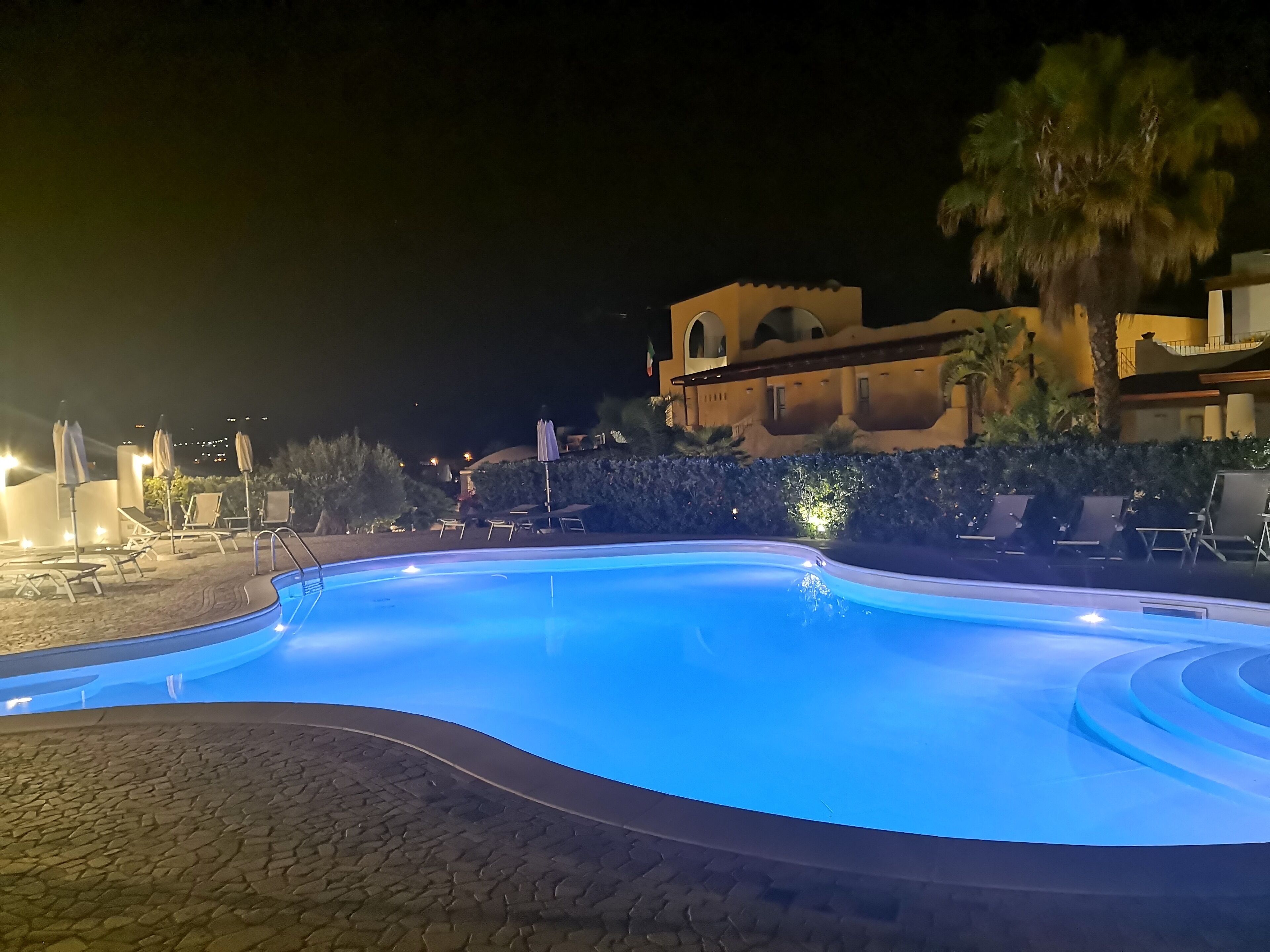 Ein Pool bei Nacht mit Liegestühlen und Sonnenschirmen darum.