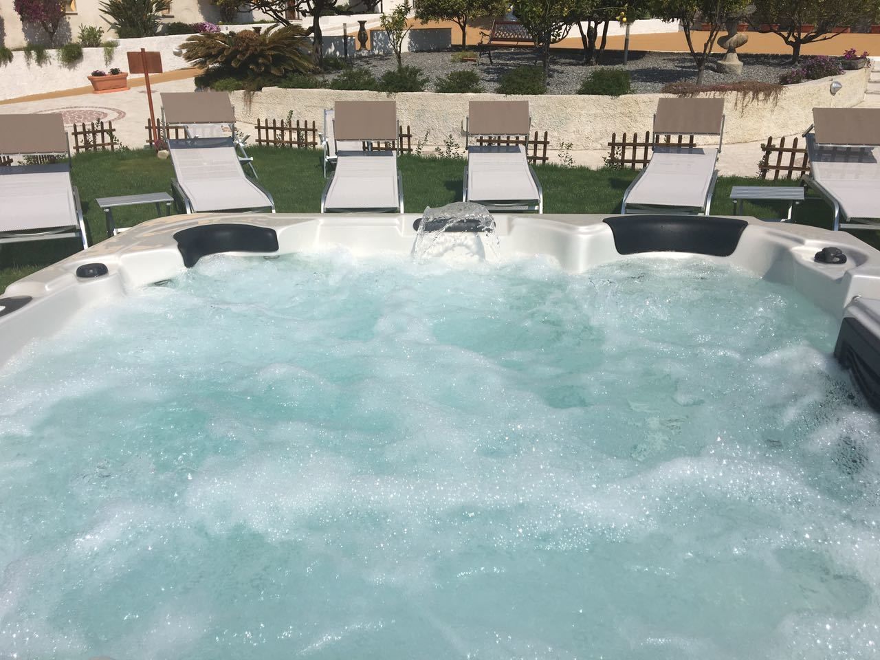 A hot tub surrounded by lounge chairs and a wooden fence.