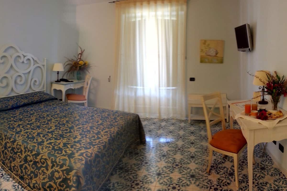 A bedroom with a bed, a chair, a small table with a lamp, and a TV on the wall.