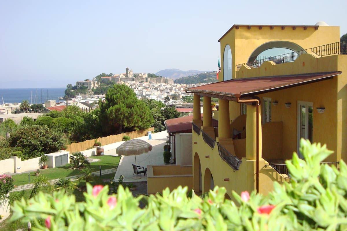A yellow building with a balcony, a patio with a table and chairs, and a view of a coastal town.