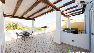 Un patio cubierto con una mesa y sillas, vista del paisaje y una puerta a la derecha.
