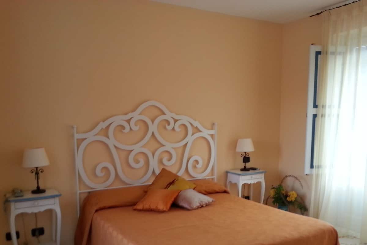 A bedroom with a bed, two bedside tables, a nightstand, and a window with curtains.