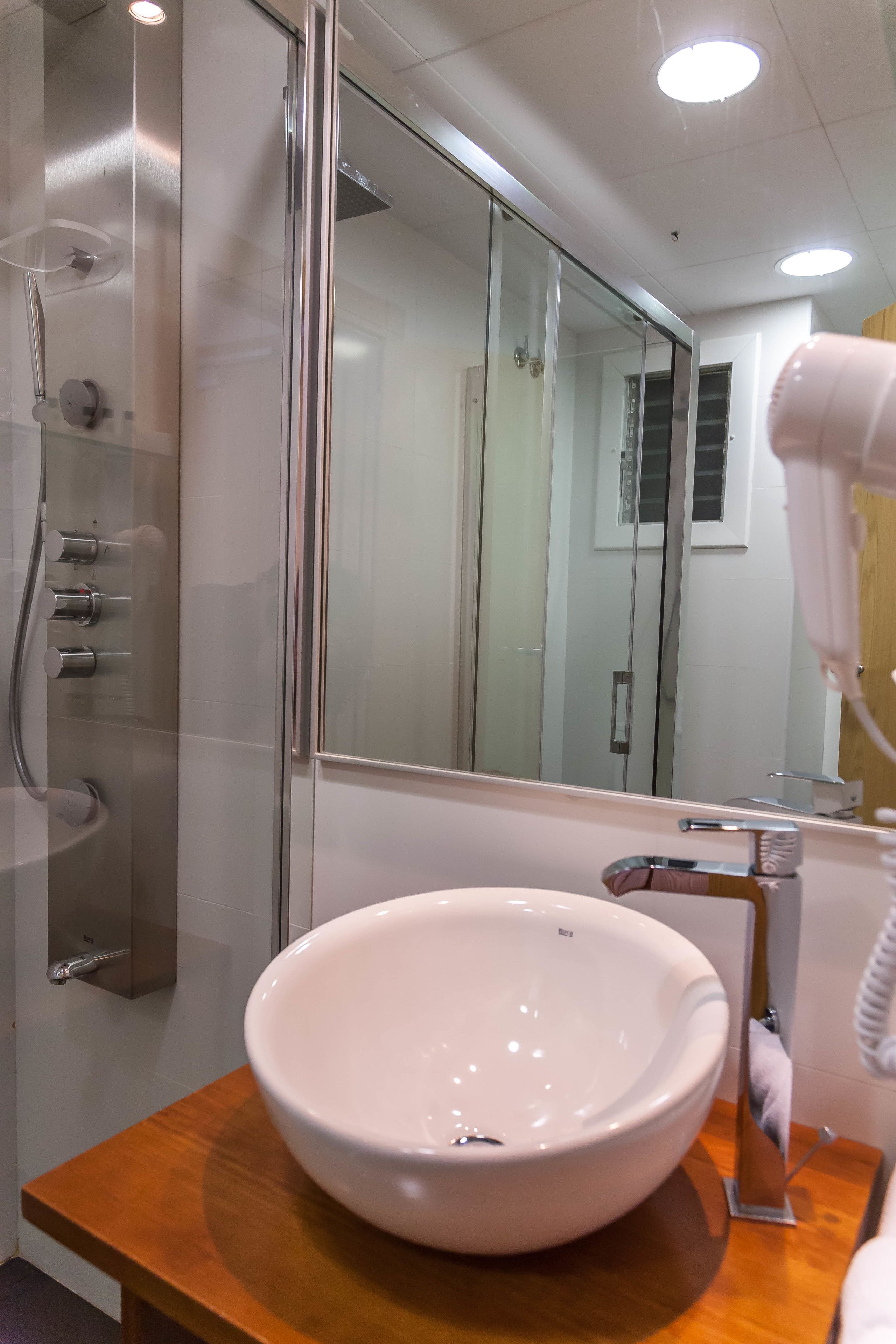 A modern bathroom with a large mirror, a white sink, and a glass-enclosed shower.