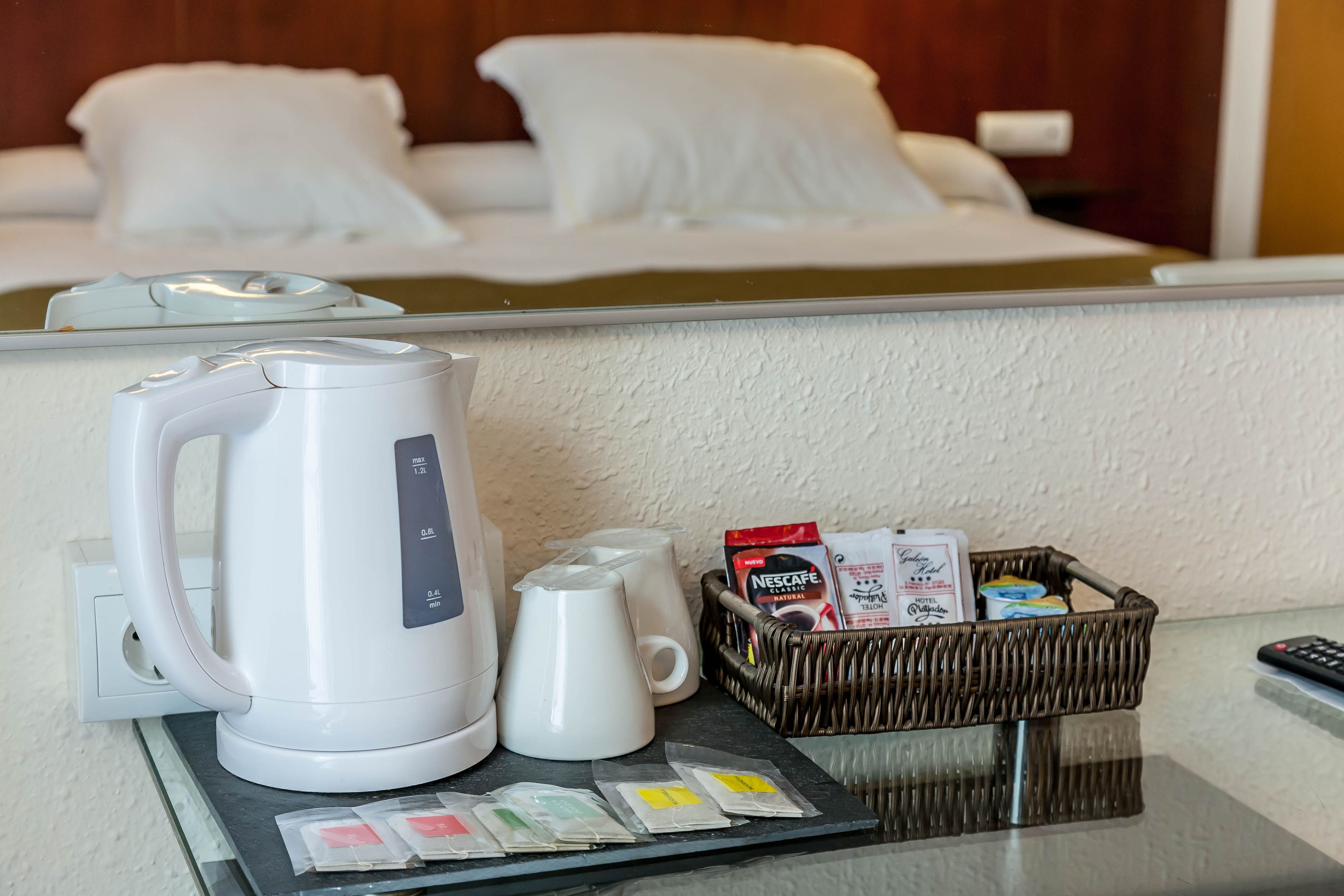 Habitación de hotel con cama, hervidor, cafetera, cesta de artículos de aseo y bandeja con sobres de té.