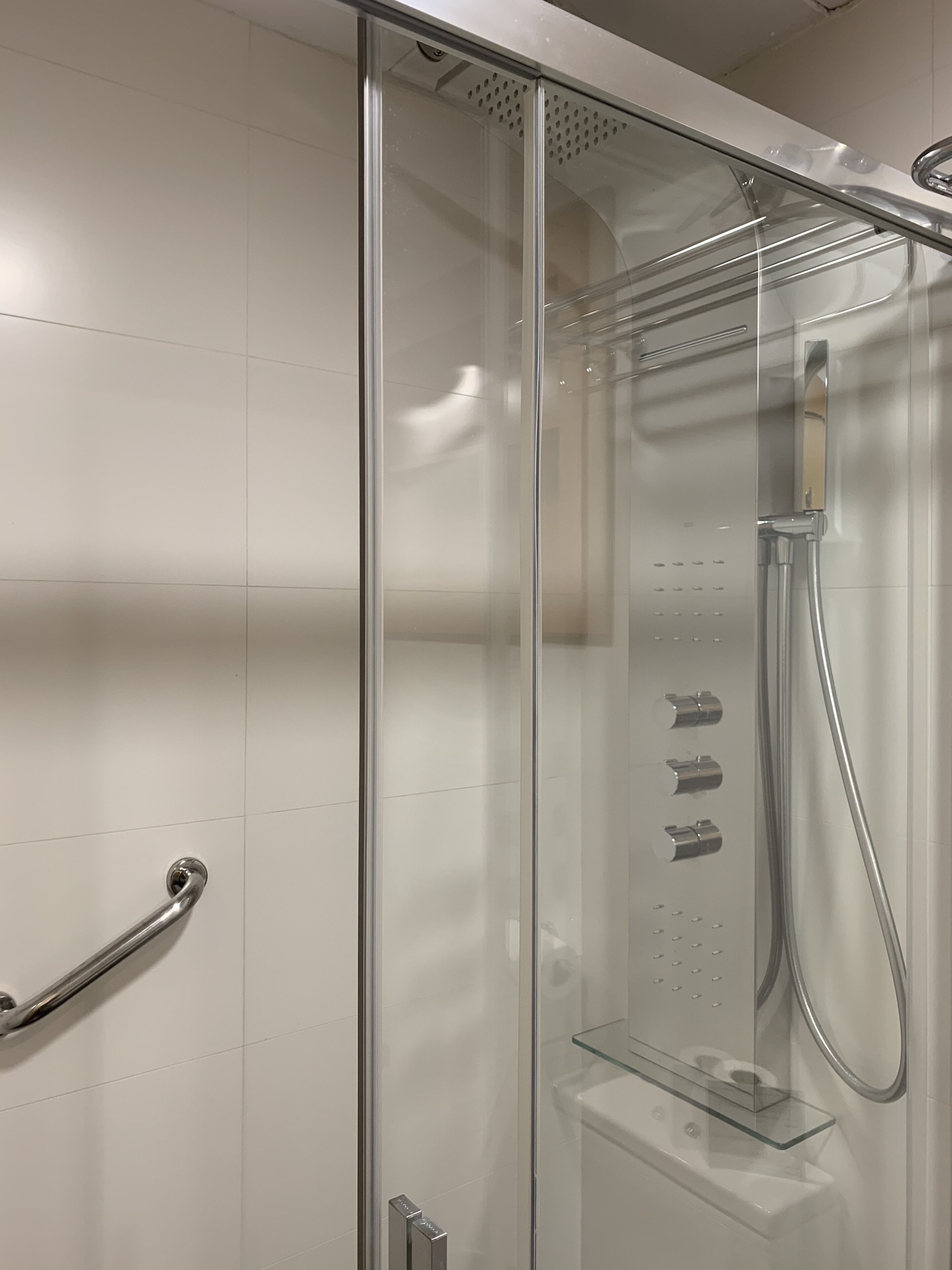 A glass-enclosed shower with a handheld showerhead and a wall-mounted faucet.