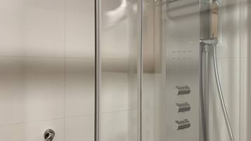 A glass-enclosed shower with a handheld showerhead and a wall-mounted faucet.