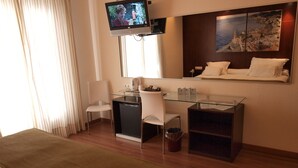 Habitación de hotel con cama, escritorio con dos sillas, televisor montado en la pared y un cuadro sobre la cama.